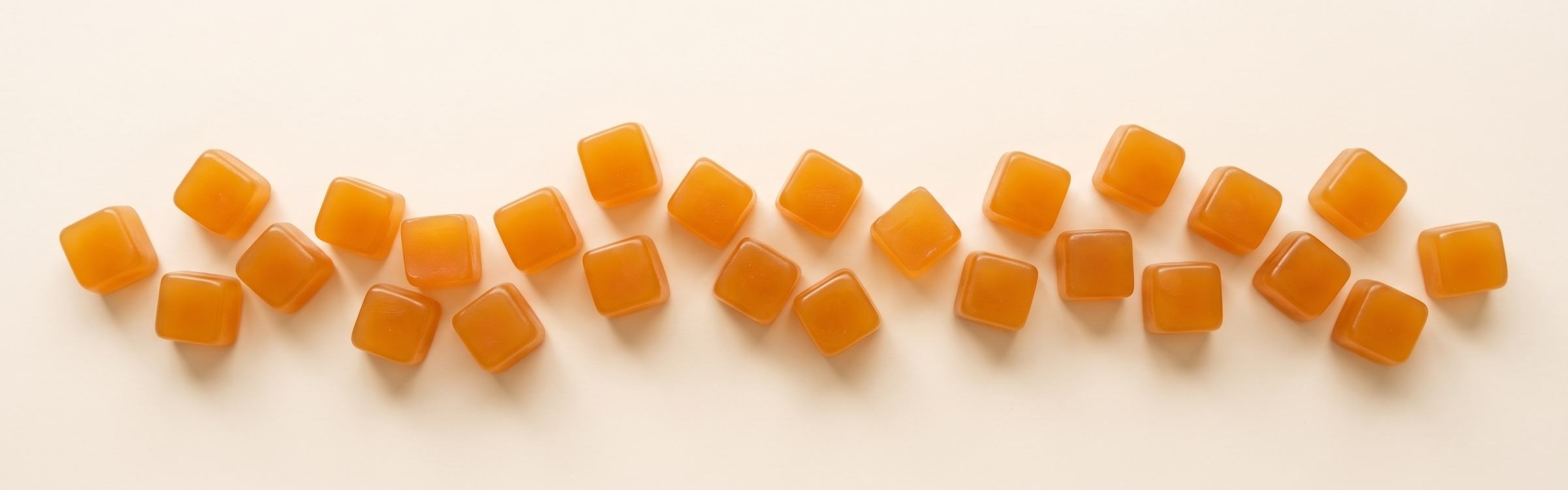 A winding line of Mango Rush gummies on cream linen